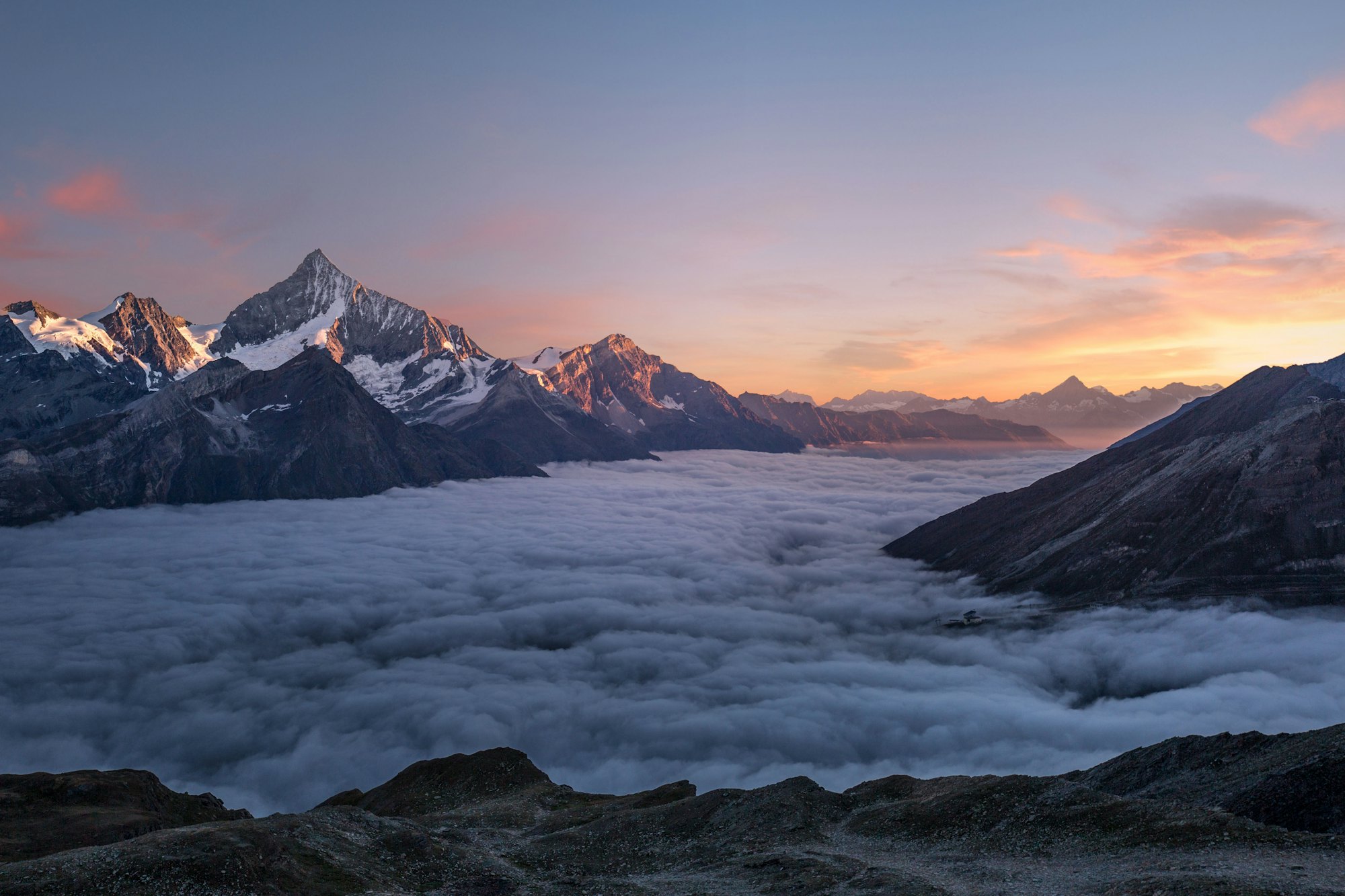 Snow peaks above a sea of cloud at sunrise in the mountains