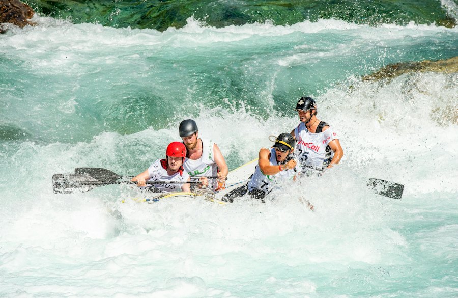A team of rafters in helmets paddling through white water